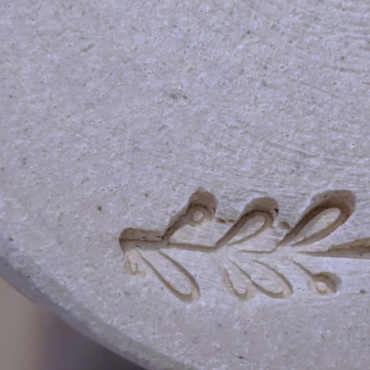 a close up of the stamp on a clay plate made in a pottery class